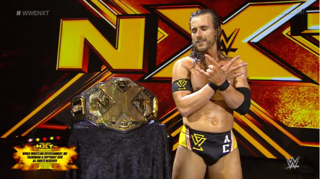 Cole stands by the nXt title, on the stage, holding the Undisputed Era hand symbol.