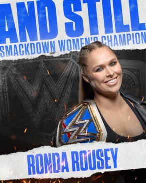 Ronda Rousey smiles with the Smackdown Women's Championship belt over her shoulder. A graphic of the championship, in black, is behind her, with the words "And Still" in blue above her.