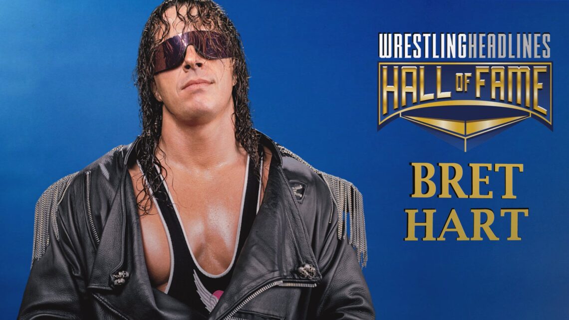 Bret Hart has his trademark black shades on that fully cover his eyes and eyebrows. Curled black hair falls over his face and down to just past his shoulders. He is wearing a black leather jacket with very fine chains hanging from the shoulders.